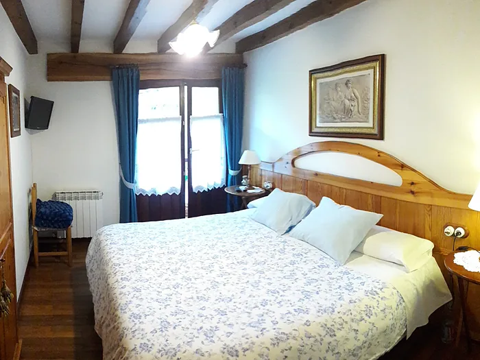 Habitación doble con cabecero de madera, colcha clara y ventana al campo.