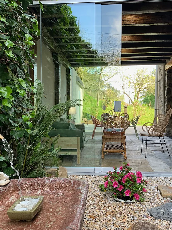 El porche exterior con muro de piedra, plantas y sillas de mimbre.
